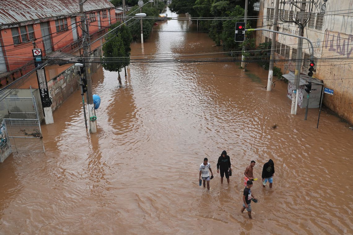 Pessoas caminham por uma rua inundada após fortes chuvas no bairro de Vila Prudente, em São Paulo.